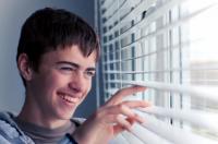 Happy young boy looking through window blinds